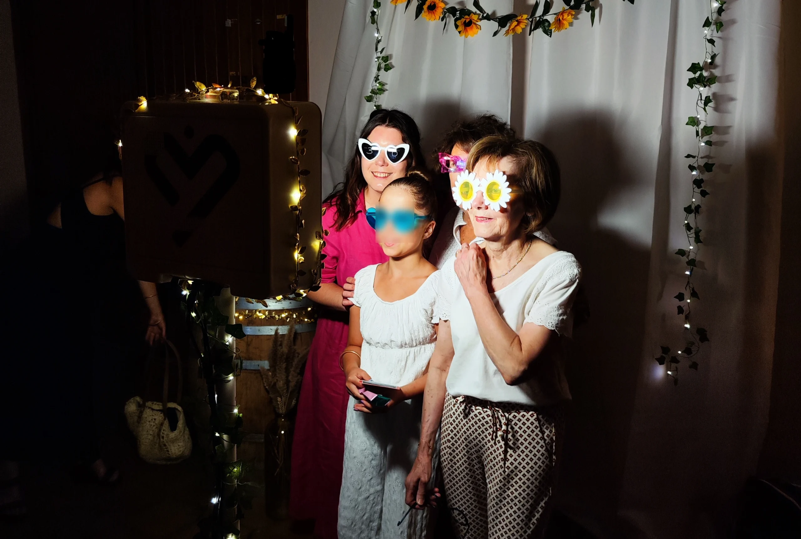 Invités posant avec des accessoires photobooth devant un décor fleuri et une guirlande lumineuse, lors d’un événement à Beaune